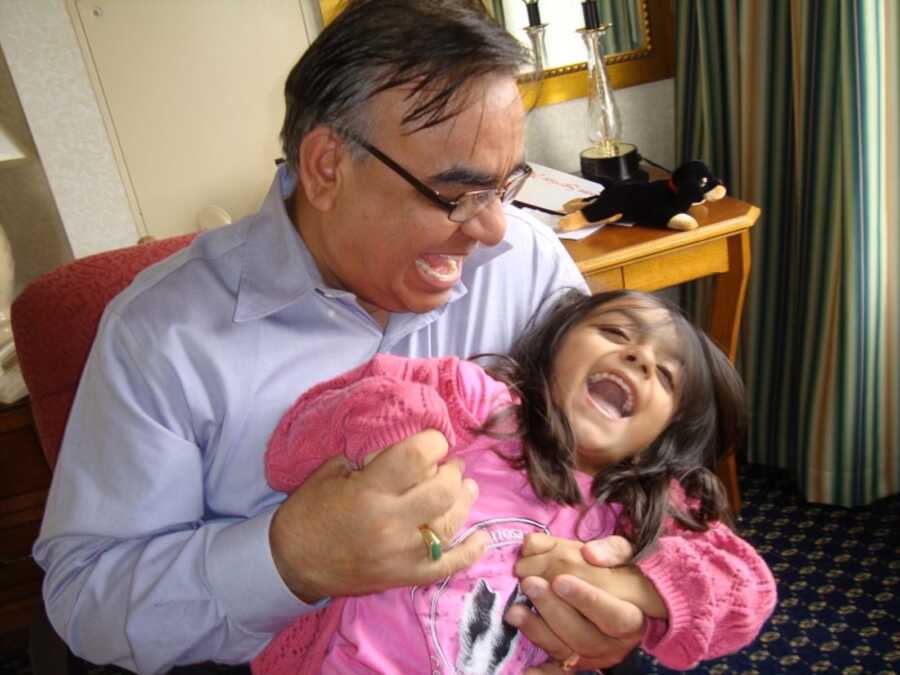 Little girl laughs as her father tickles her while holding her on his lap. 