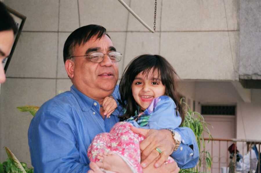 Young girl smiles as her father holds her in his arms. 