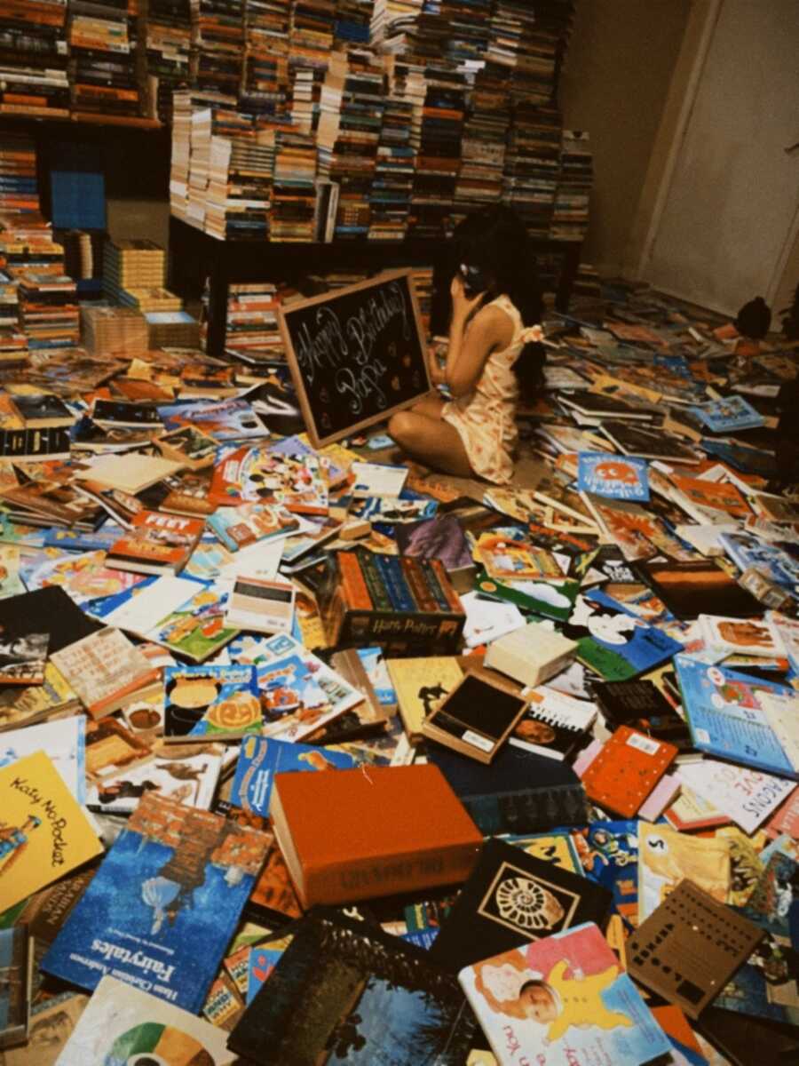 Teen girl sits on the floor surrounded by books donated for children fighting cancer.