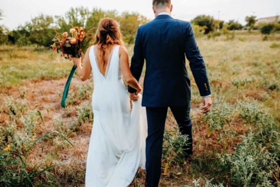 A bride and groom hold hands and walk into a field