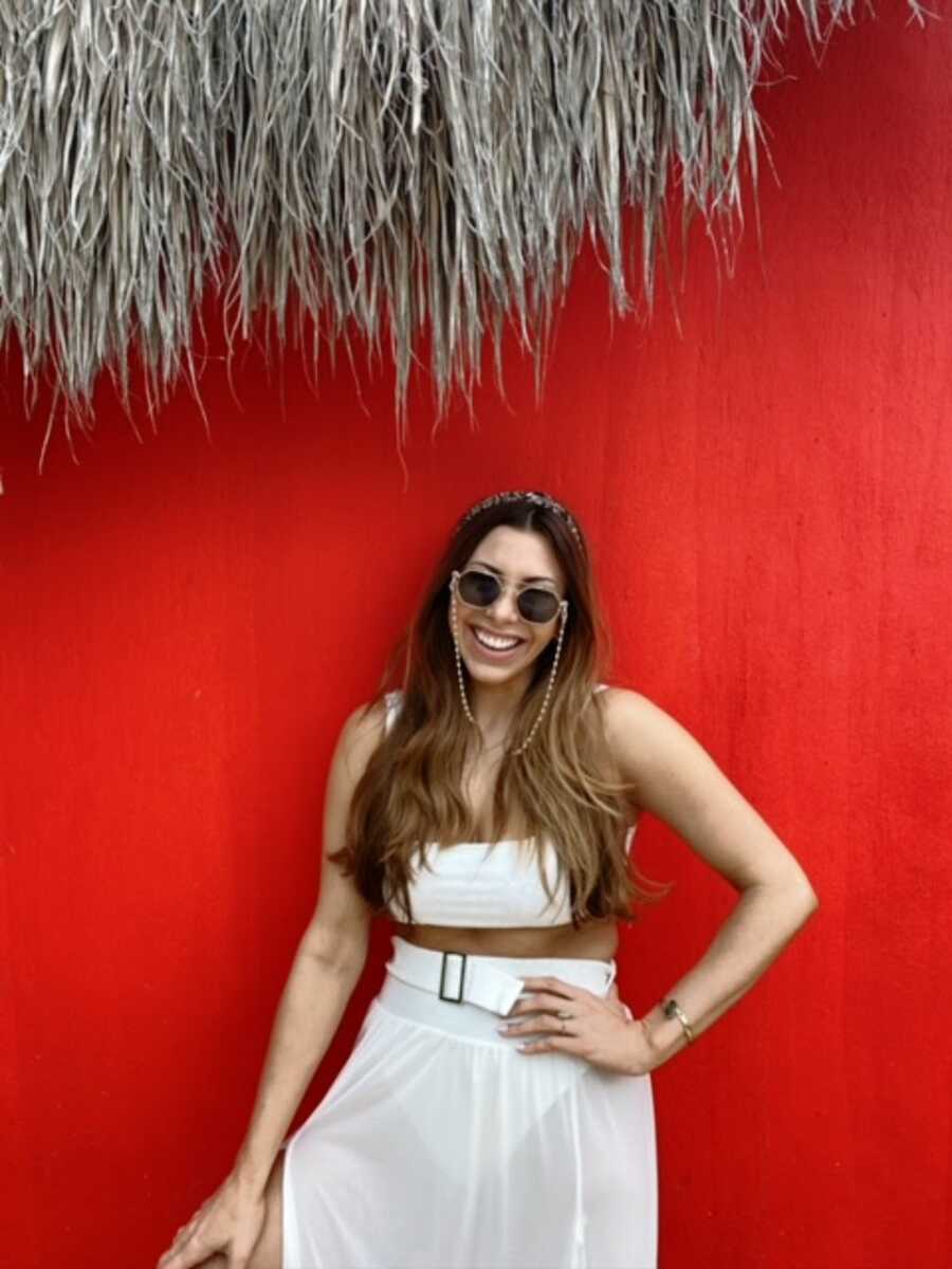 A woman wearing sunglasses stands in front of a red wall