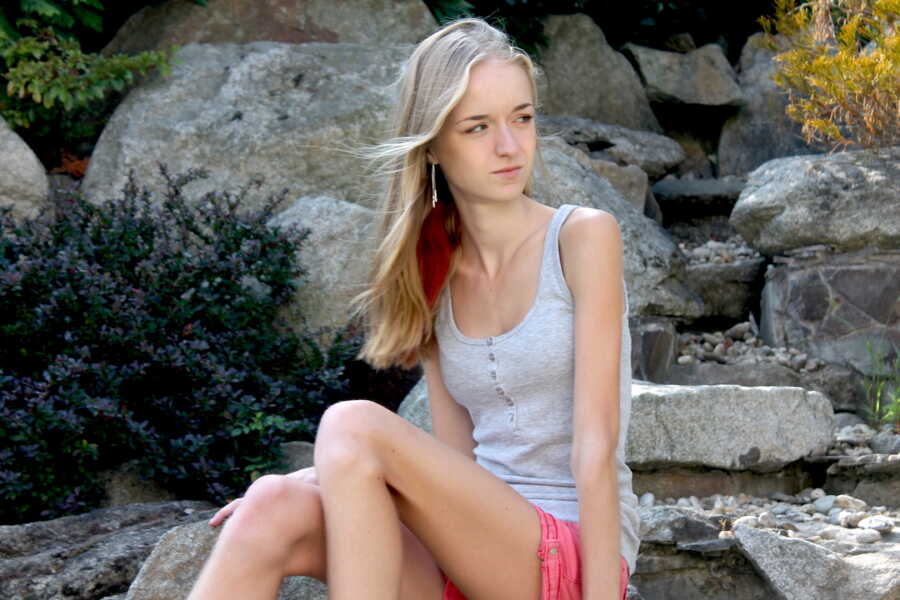 girl with anorexia sits on rocks and looks over her shoulder
