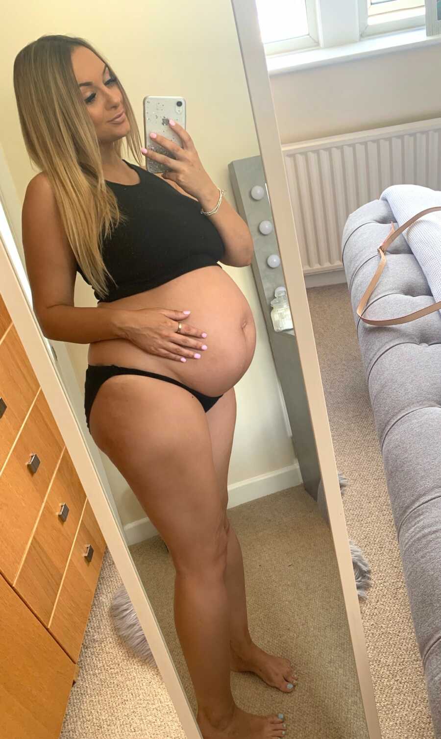 pregnant woman stands in front of mirror holding her belly