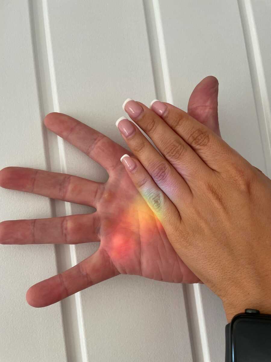 wife places her hand on top of husband's as rainbow light is reflected on them