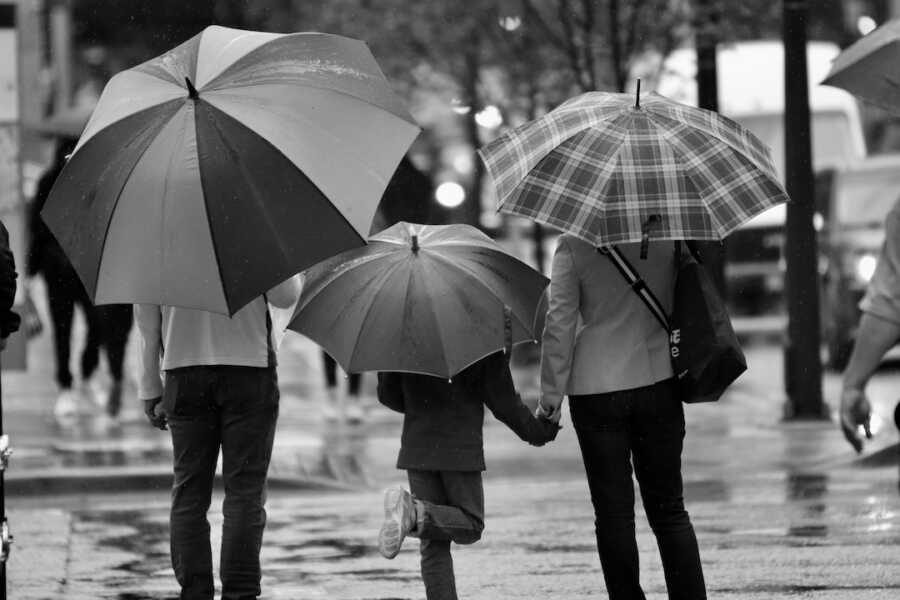 child stands between parents as they all walk holding umbrellas