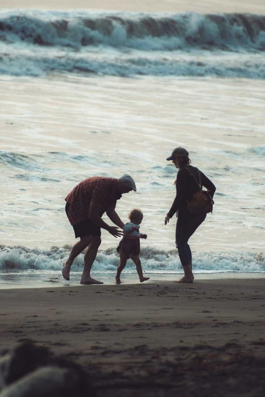 family on the beach, dad goes to hold child, mom stands by
