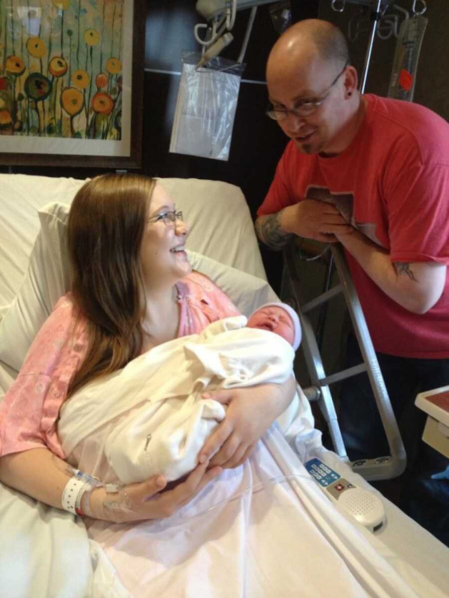 mother in hospital bed with newborn in arms with dad standing at the edge 