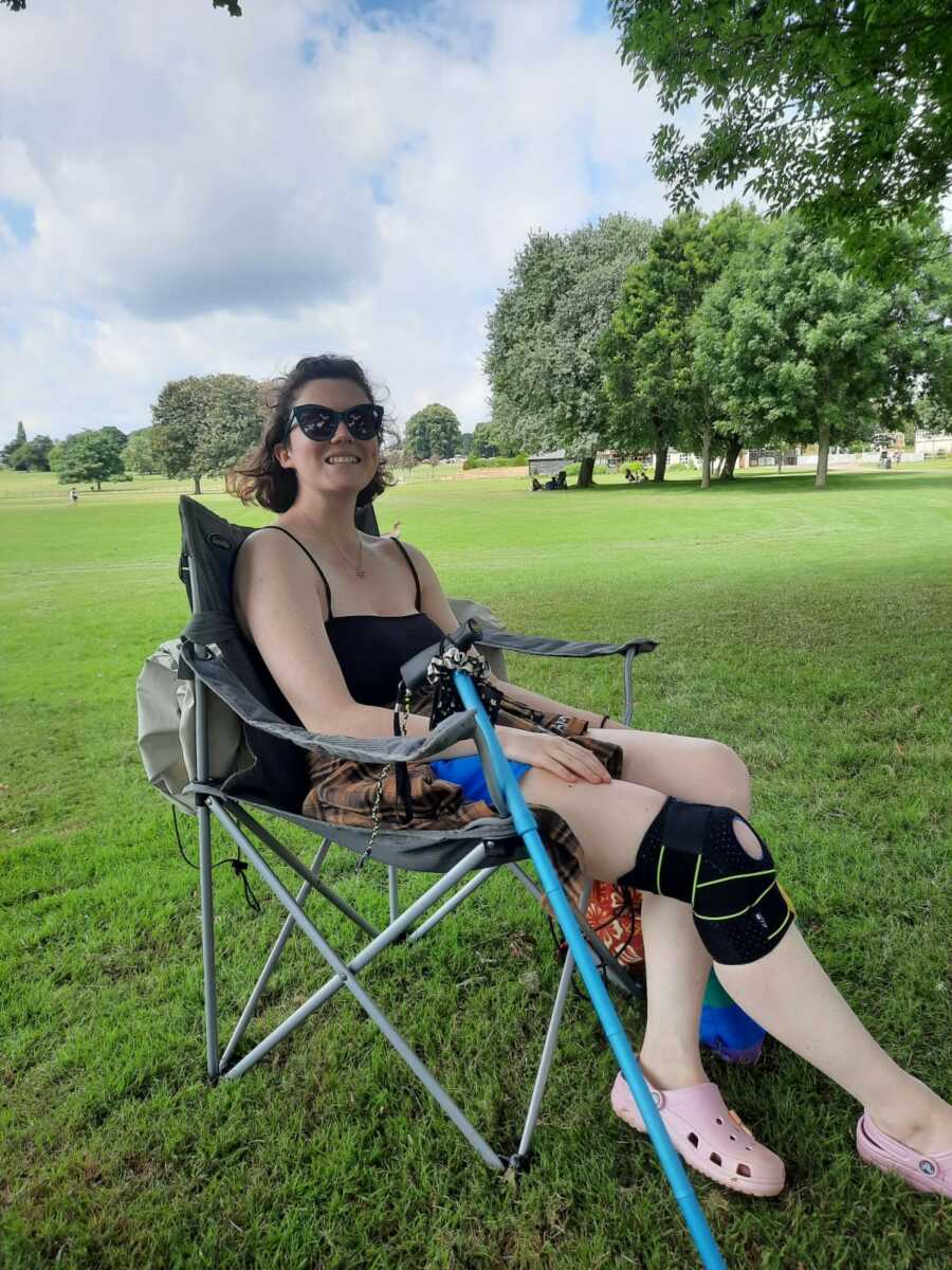 woman with disability sitting in camping chair with cane and knee brace