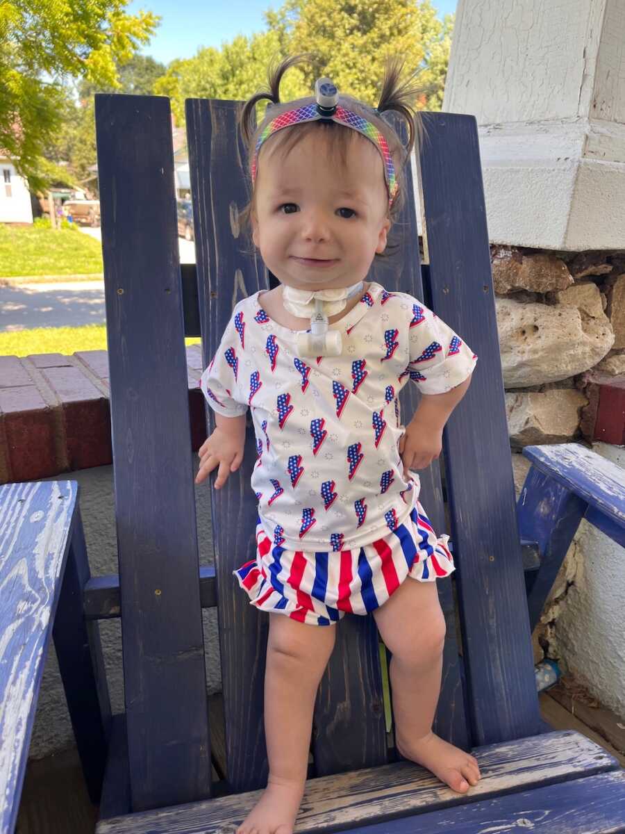 girl with nager syndrome stands on a chair smiling