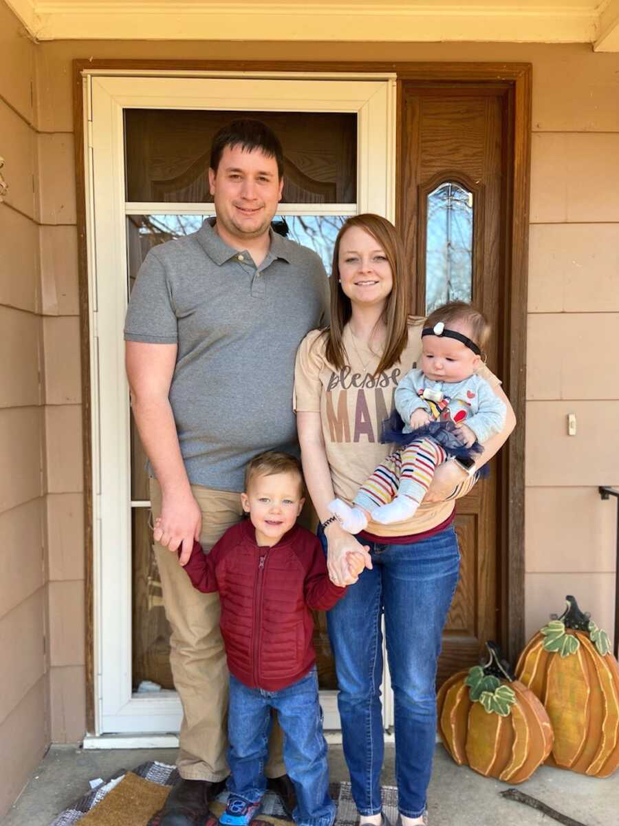 family stands together, mom holds daughter while dad holds son's hand