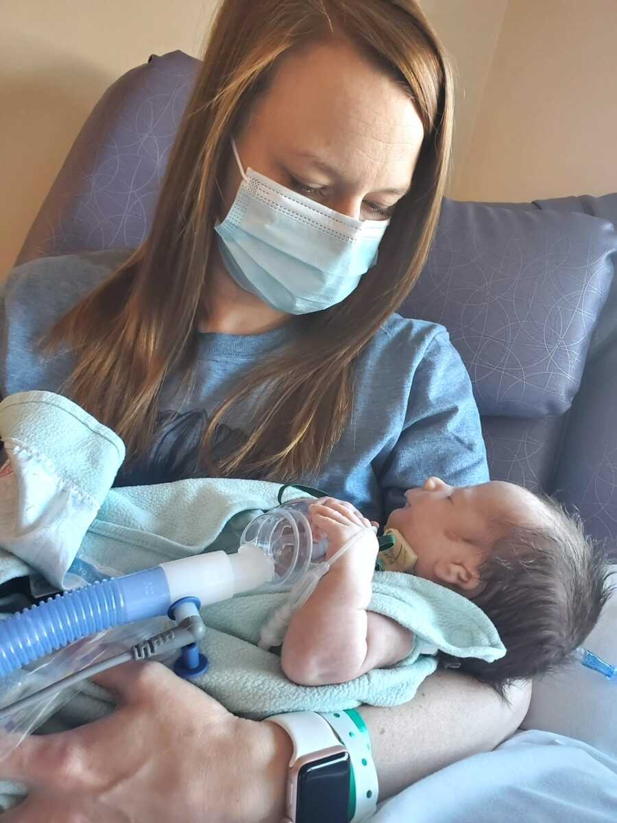 mom sits looking down at daughter in NICU who lays in her arms