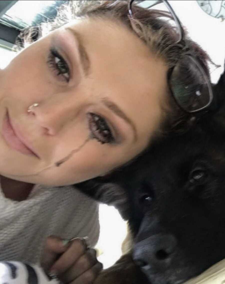 girl cries, makeup running down her face with head against dog