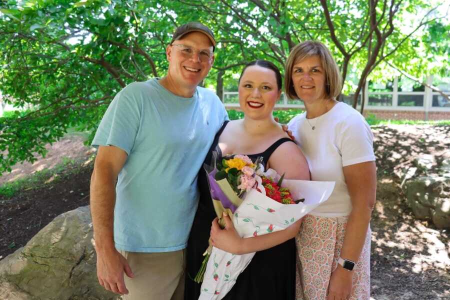 Adult ballerina poses with her parents after a recital