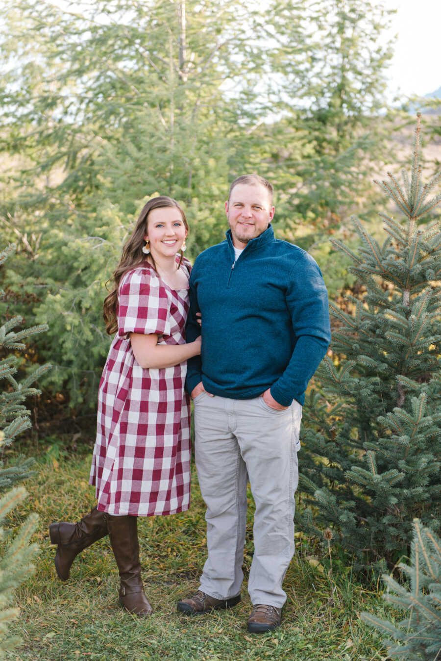 wife wraps arms around husband's arm while at tree farm