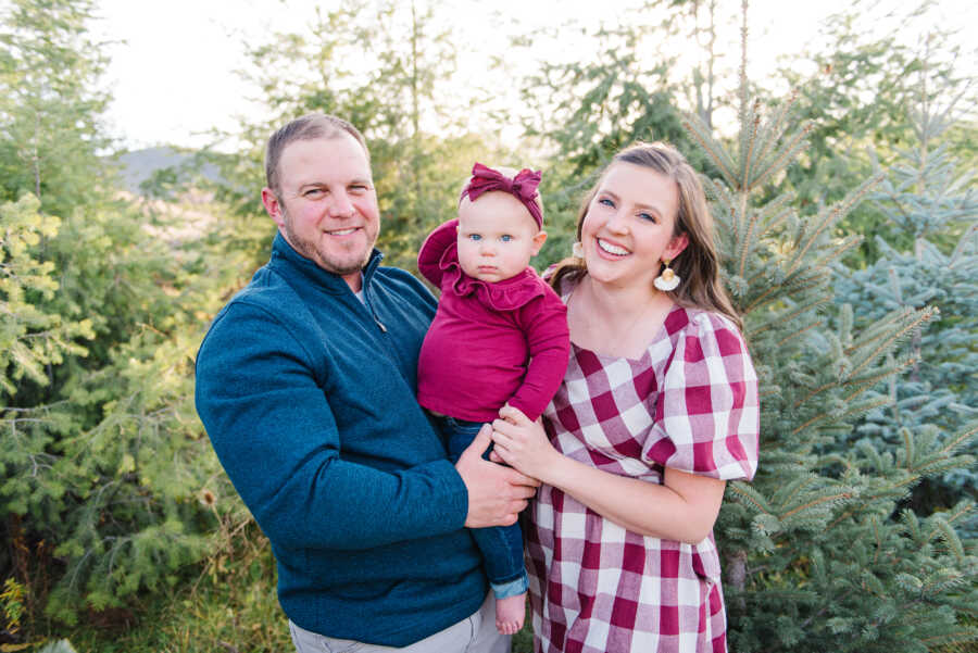 mom and dad hold their adopted daughter in a tree farm
