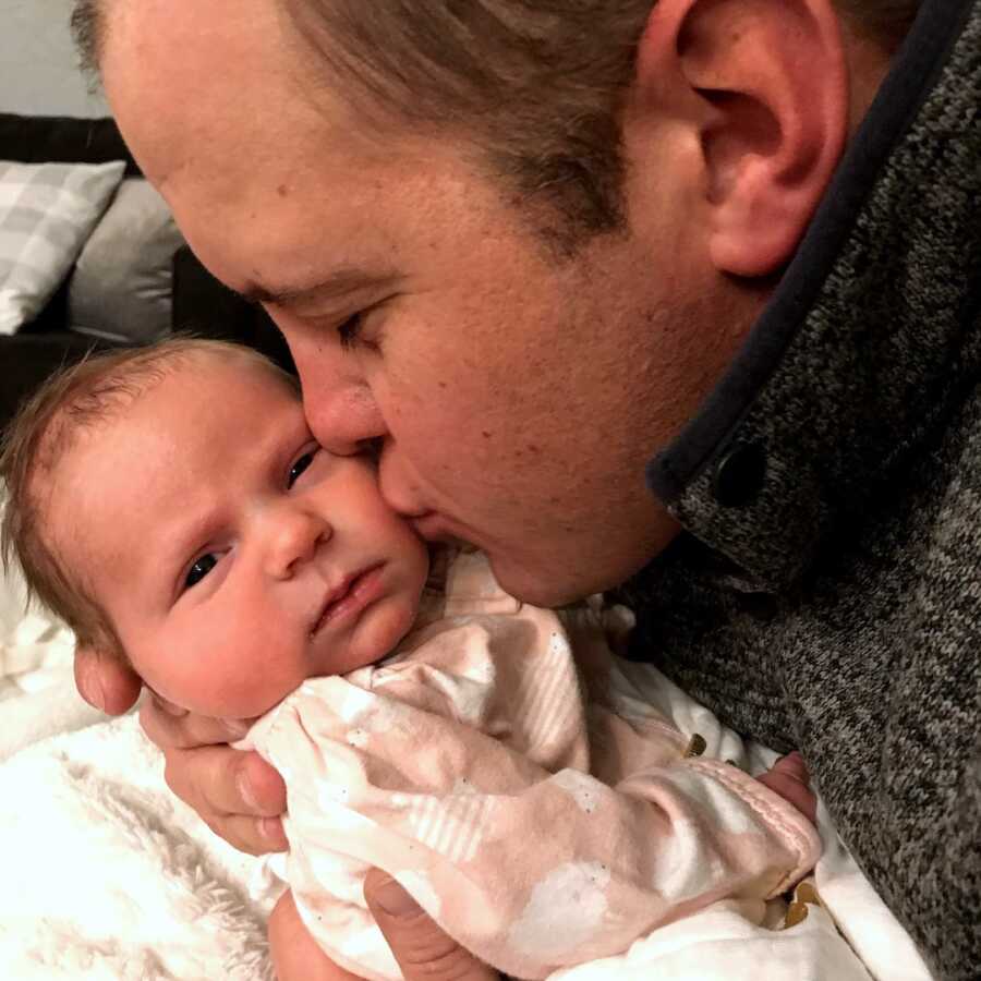 adoptive dad kisses his baby girl on the cheek gently