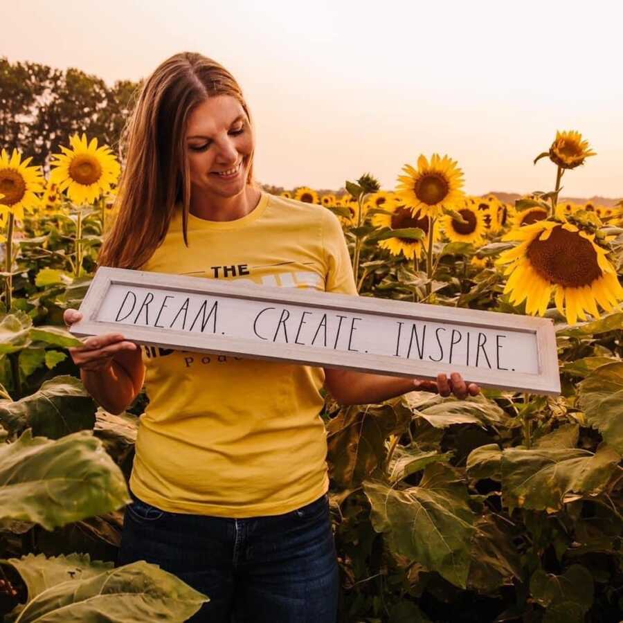 A woman poses with a sign that says 'dream. create. inspire"
