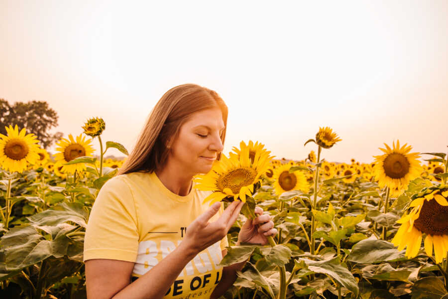 A woman smells a sunflower in a field 