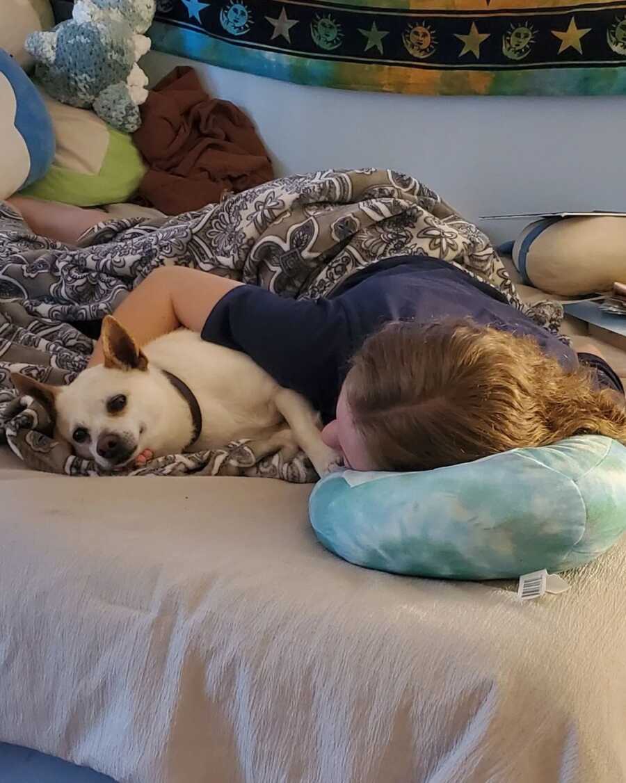 Teen girl snuggles with her arm around her dog while lying in bed.