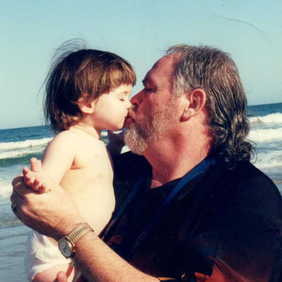 A dad kisses his baby daughter at the beach