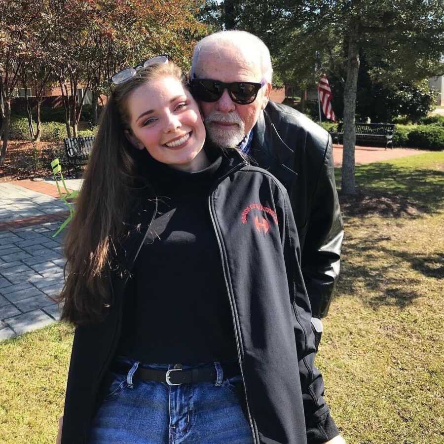 A girl and her father stand in a grassy park