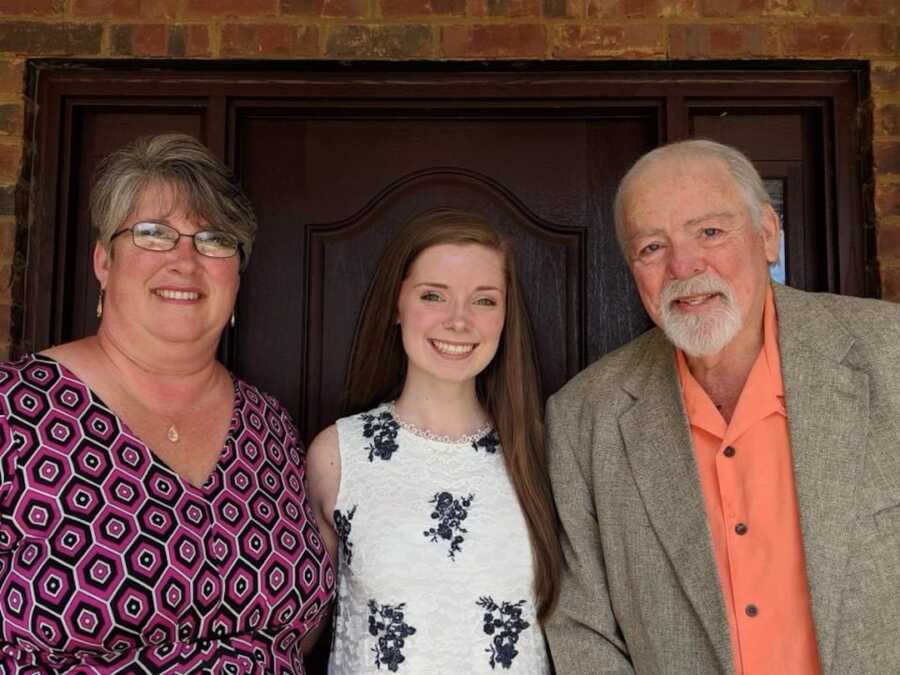 A young girl stands with her parents in nice clothes