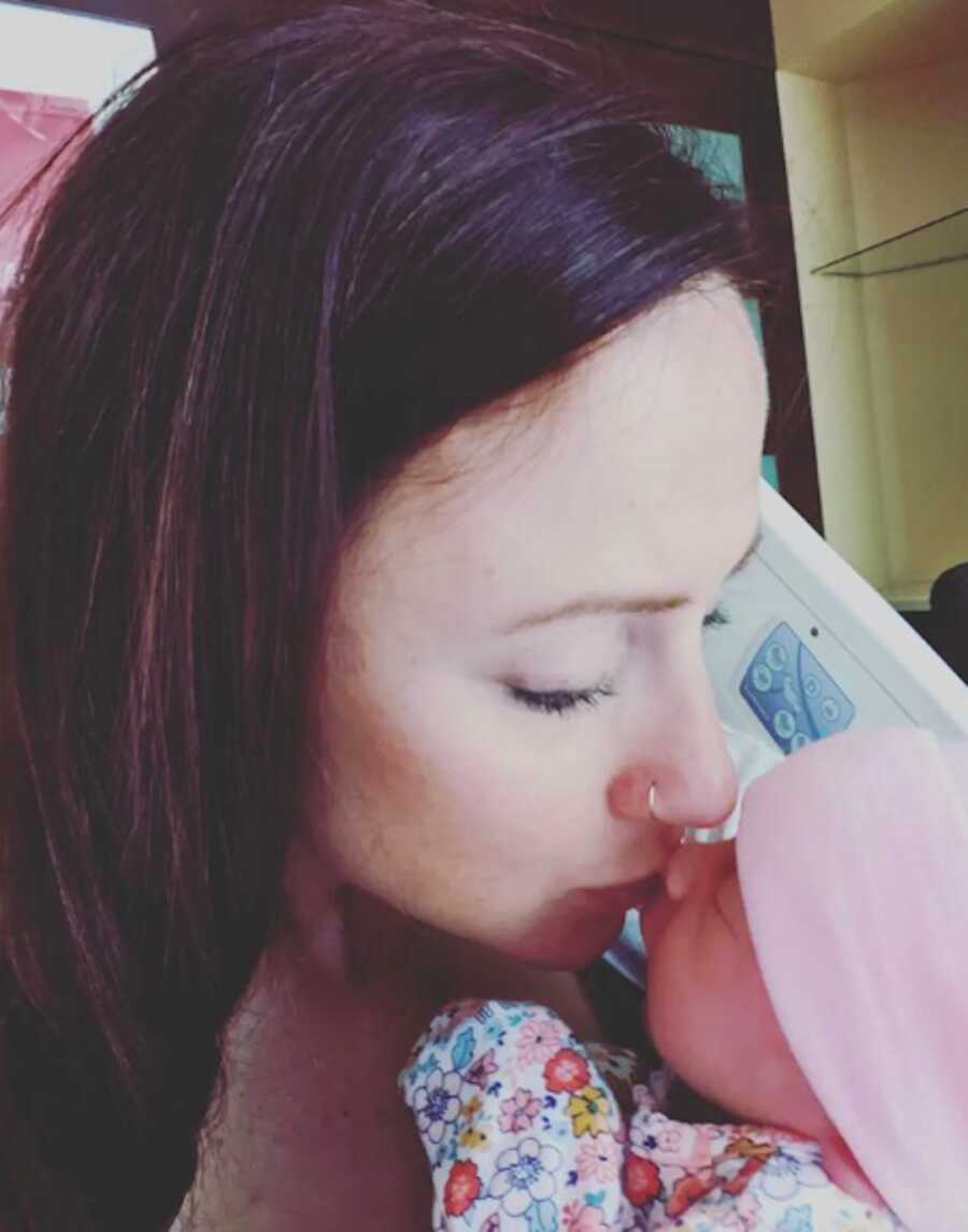 mother kissing baby in hospital bed