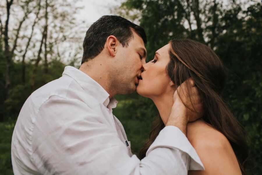 husband and wife kiss one another while husband has hand on wife's face