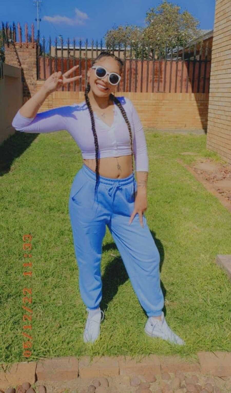 A woman stands outside wearing a crop top and blue pants