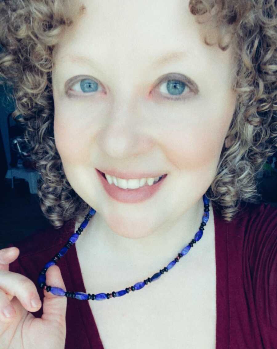 A jewelry-maker holds handmade necklace she's wearing