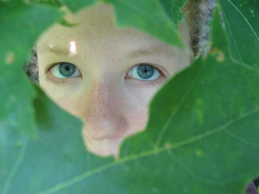 A woman peers through a hole in some leaves