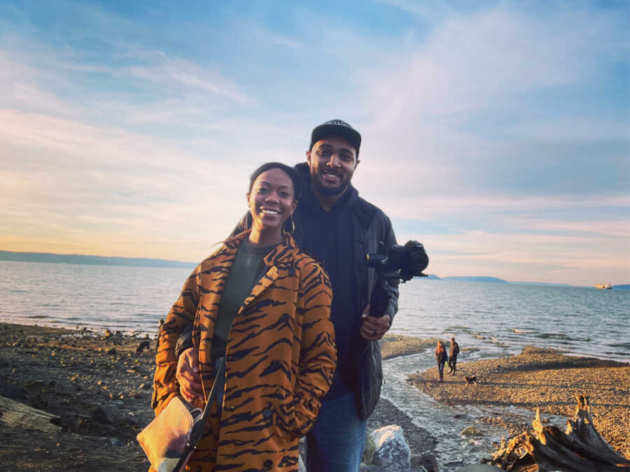 Black couple stand in front of a sunset over the water