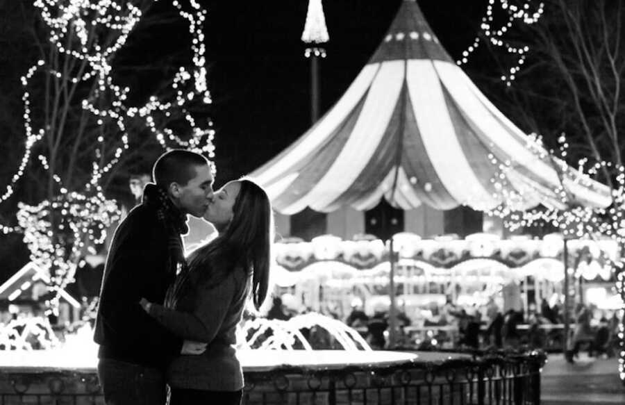 couple stands at a fair with lights behind them as they kiss