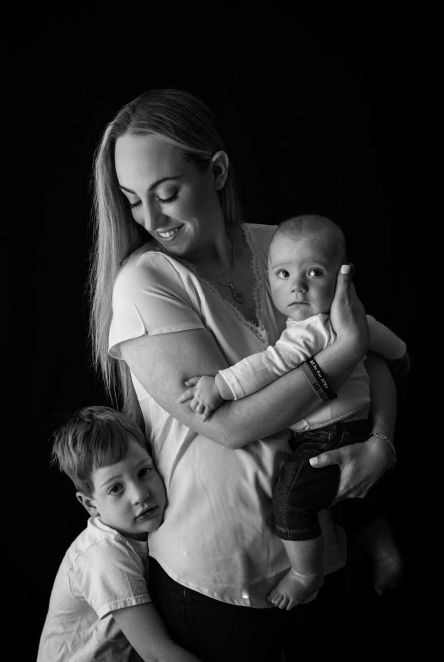 mom holds her younger son while the older holds onto her and she looks down at him