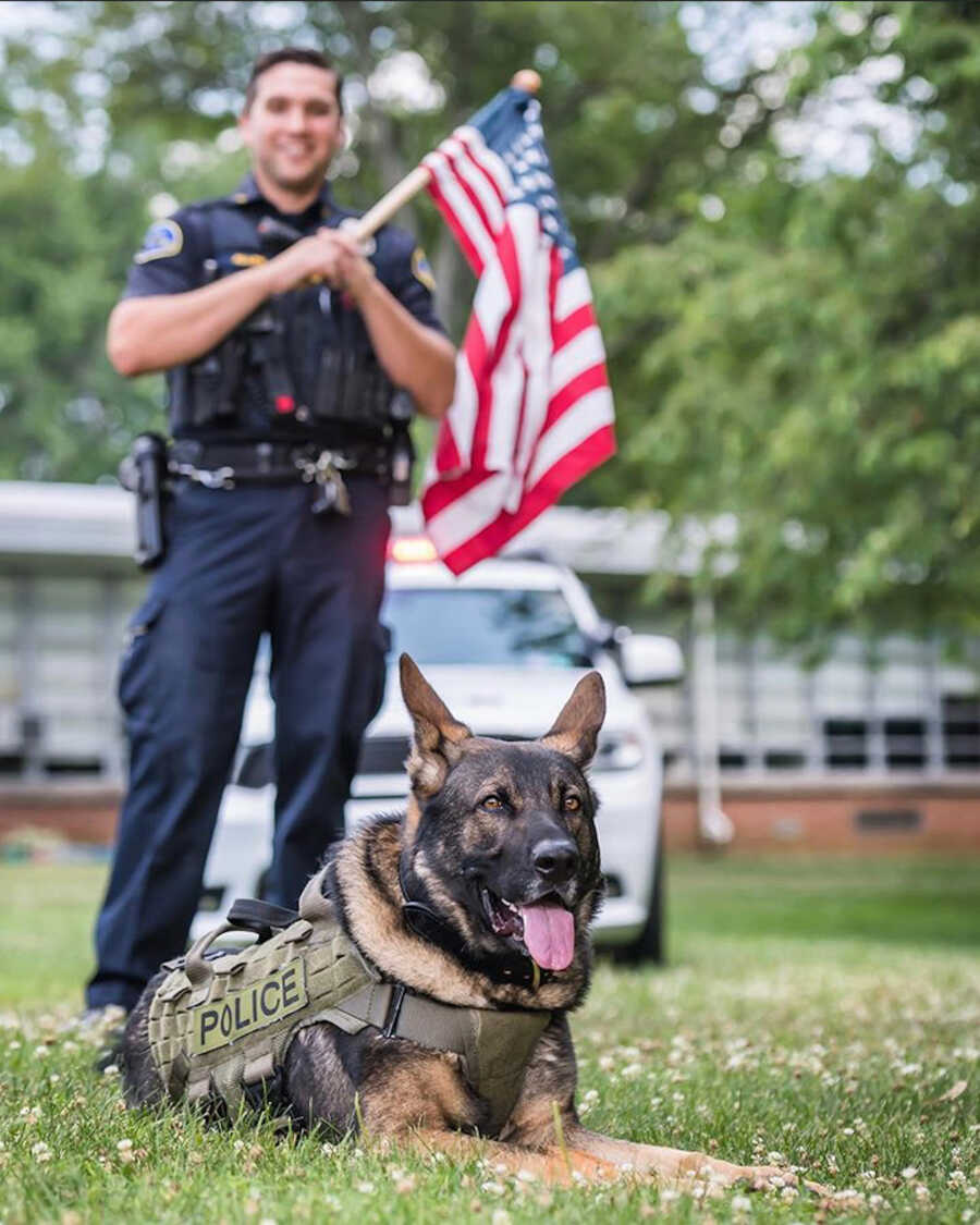 police officer stands behind his k9 holding an American flag