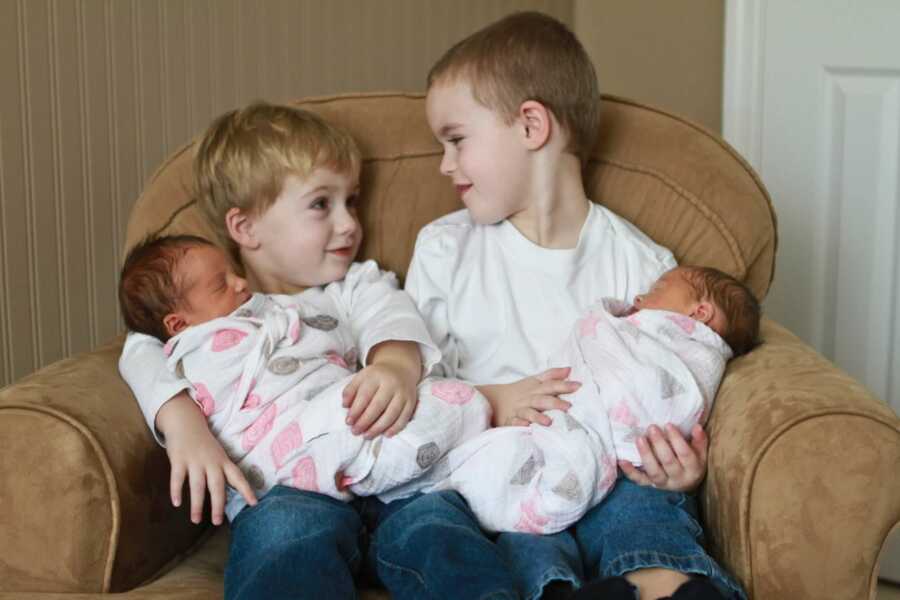 big brothers hold their twin baby sister on their laps