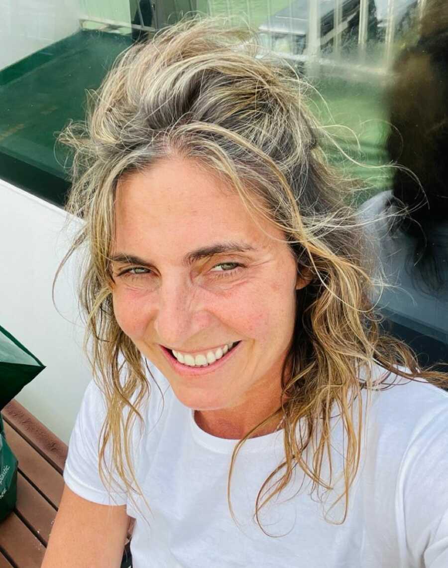 Bulimia and sexual abuse survivor wearing a white is sitting on a bench smiling at camera