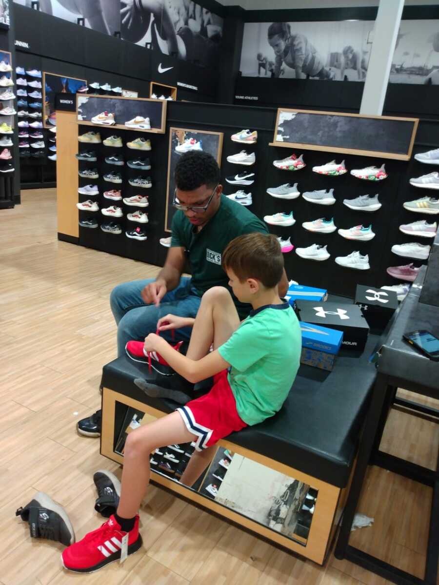 Little boy tying shoelaces with shoe sales associatein a shoe store