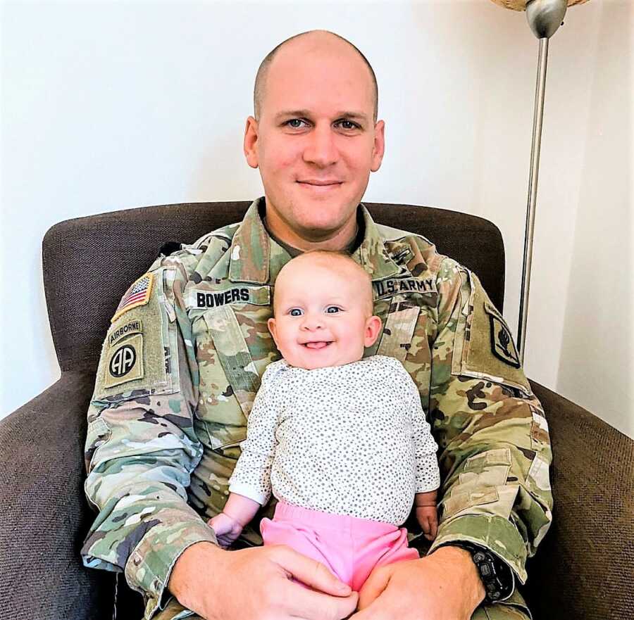 Military husband sitting on a chair with his baby daughter on his lap 