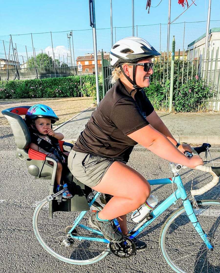 Military wife going on a bike ride with her toddle daughter in the back seat 