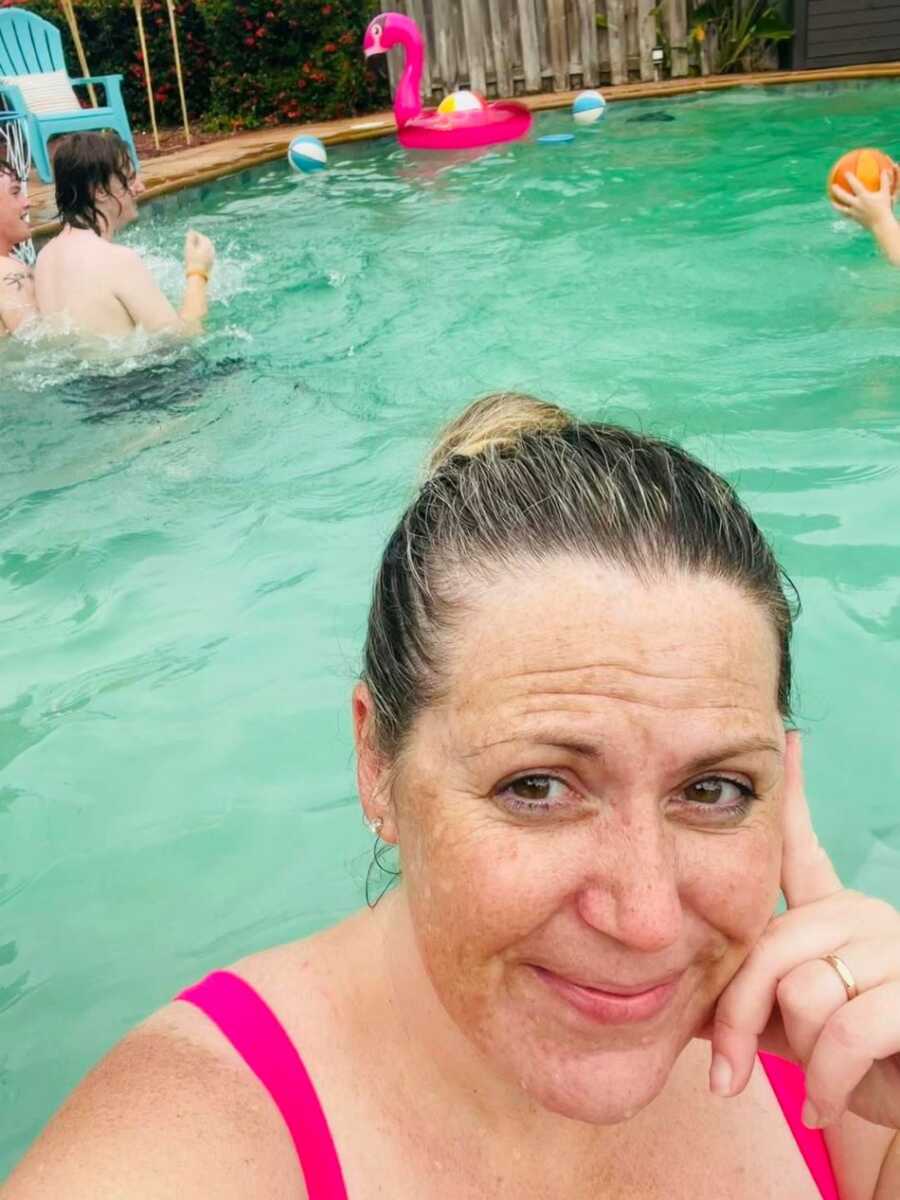 Mother taking selfie in pool with kids behind her