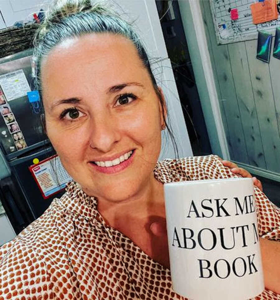 adult adoptee holding "ask me about my book" mug