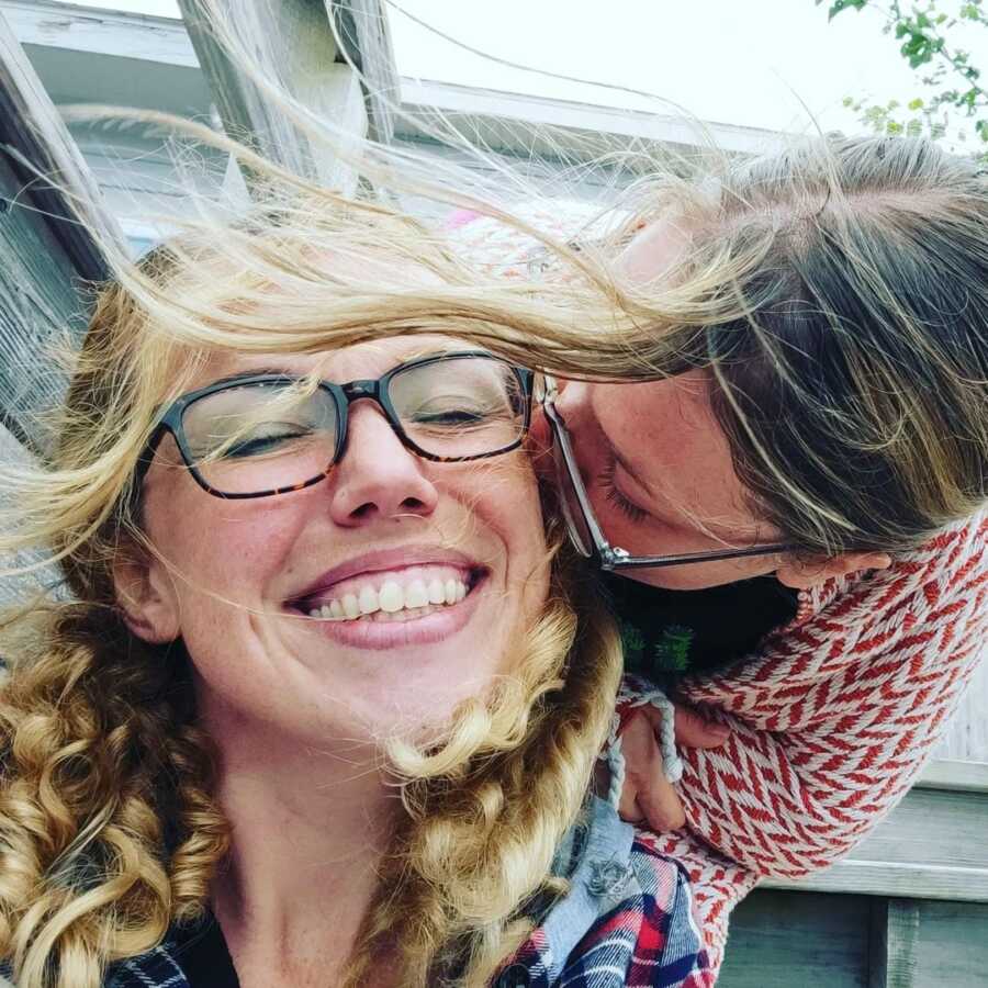 Friends kisses woman on the cheek as she closes her eyes and smiles.