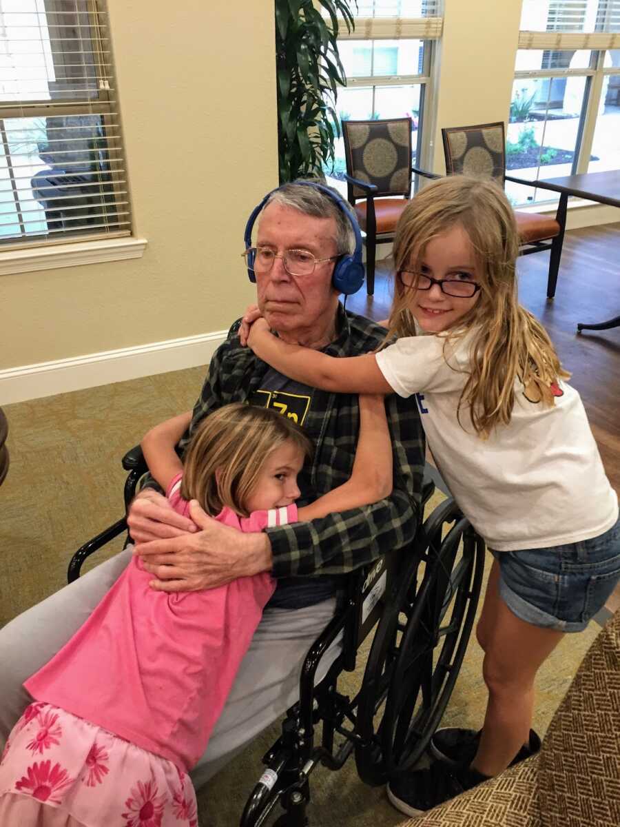 Alzheimers grandfather in wheelchair being hugged by two granddaughters
