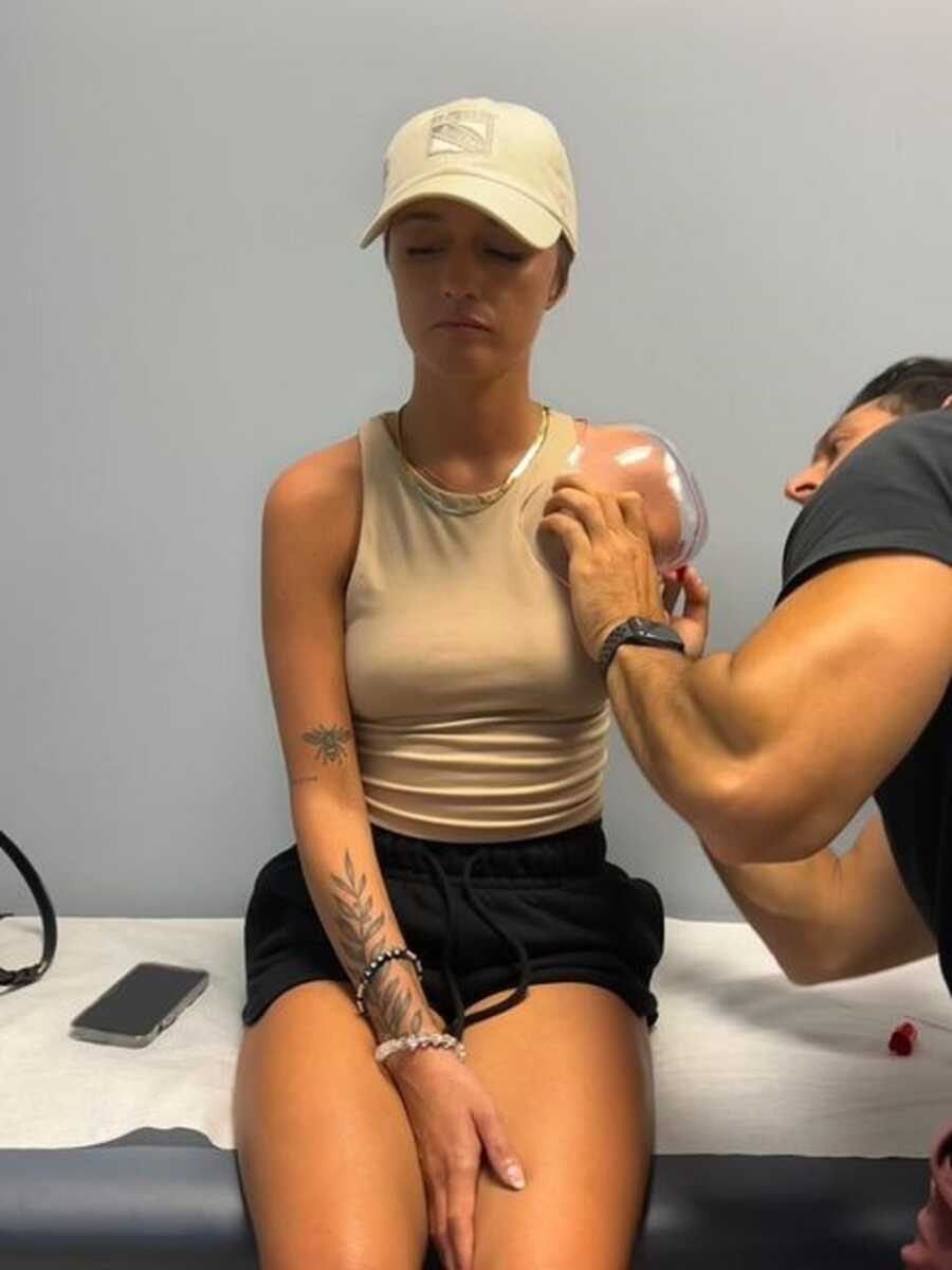 Woman sits on a hospital examination table while a nurse checks on her amputated arm.