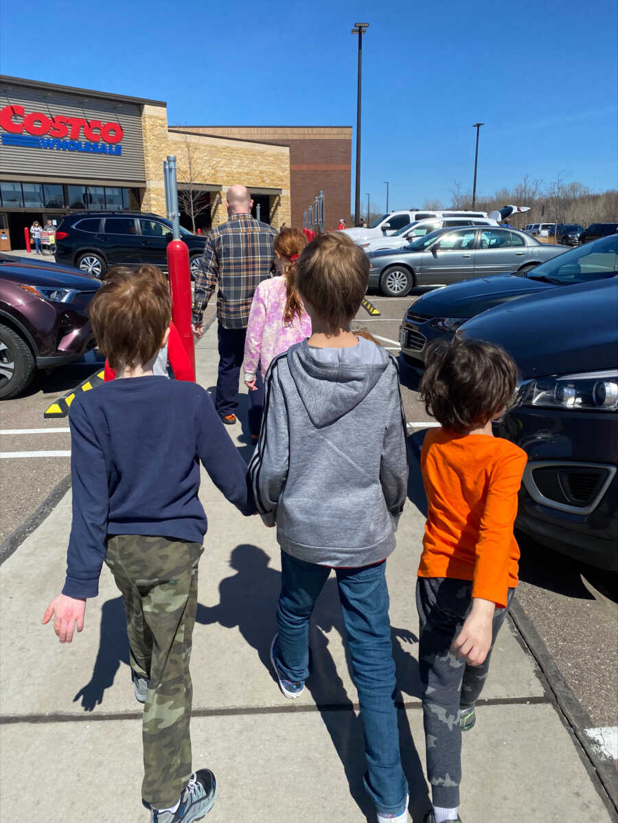 Three siblings hold hands walking down the street