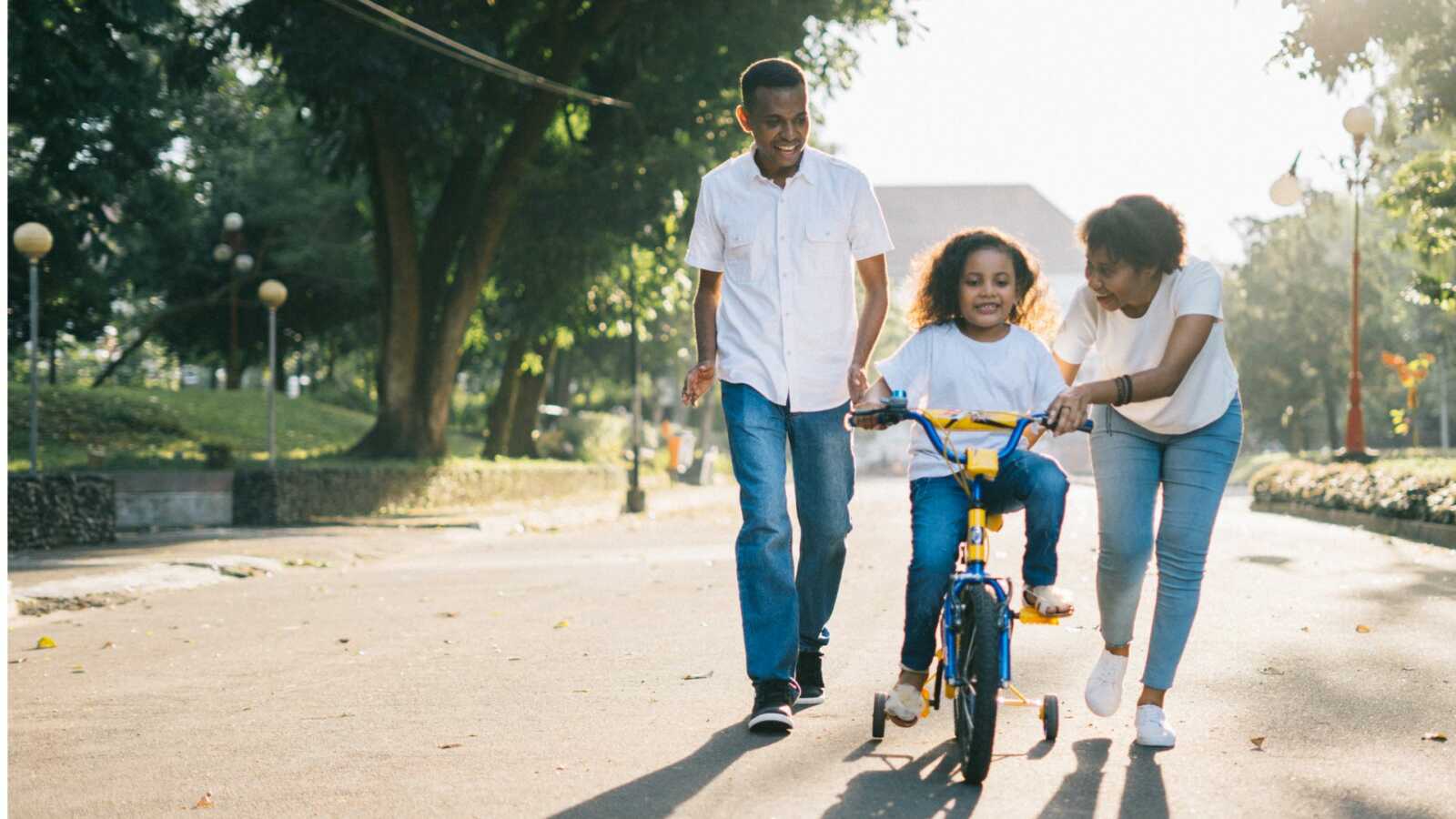 black parents coparenting daughter riding bicycle in street
