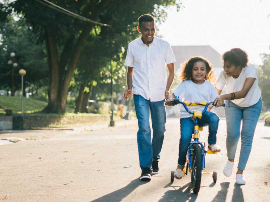 black parents coparenting daughter riding bicycle in street