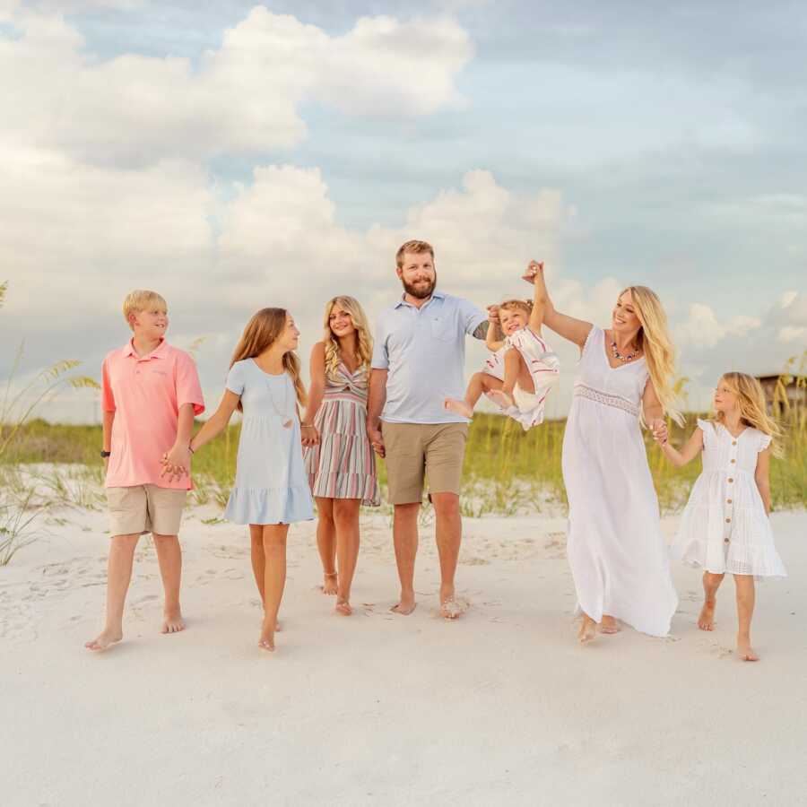 Blended family walks hand in hand on the beach