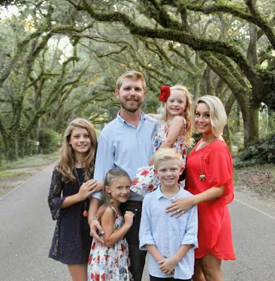 Blended family poses together under trees 